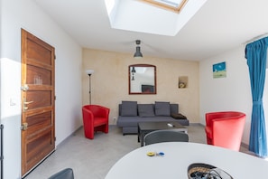 A room with a wooden door, a grey sofa, red chairs, a table, and a ceiling light. - 4 - Heart of the village F3 - air-conditioned (Charleval)