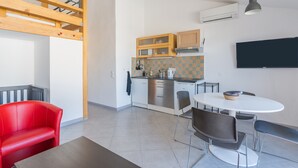 Cozinha moderna com área de refeições, um sofá vermelho e uma TV fixada na parede.