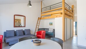 Um interior moderno com uma cama mezanina, um sofá, uma mesa de jantar e uma cadeira vermelha.