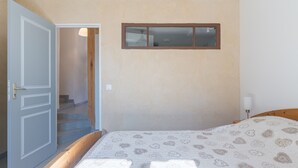 Quarto com cama, porta que dá para uma escada e uma pequena janela.