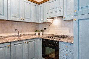 Una cocina con armarios azul claro, encimera de granito, pileta de acero inoxidable y horno empotrado.
