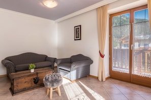 Une pièce comprenant un canapé à motifs, une commode en bois, un petit tabouret et une grande porte-fenêtre coulissante donnant sur une vue sur la montagne.