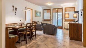 Uma sala de jantar com mesa de madeira posta para quatro pessoas, um sofá e um armário com uma luminária.