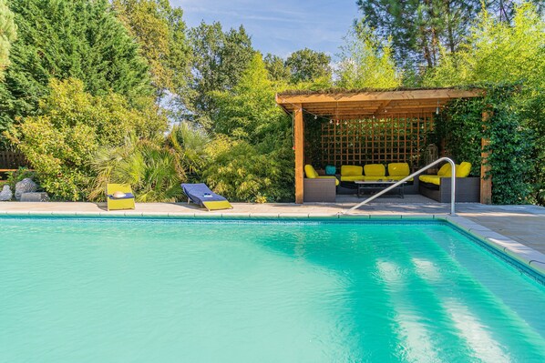 A swimming pool with lounge chairs and a wooden pergola with cushions.