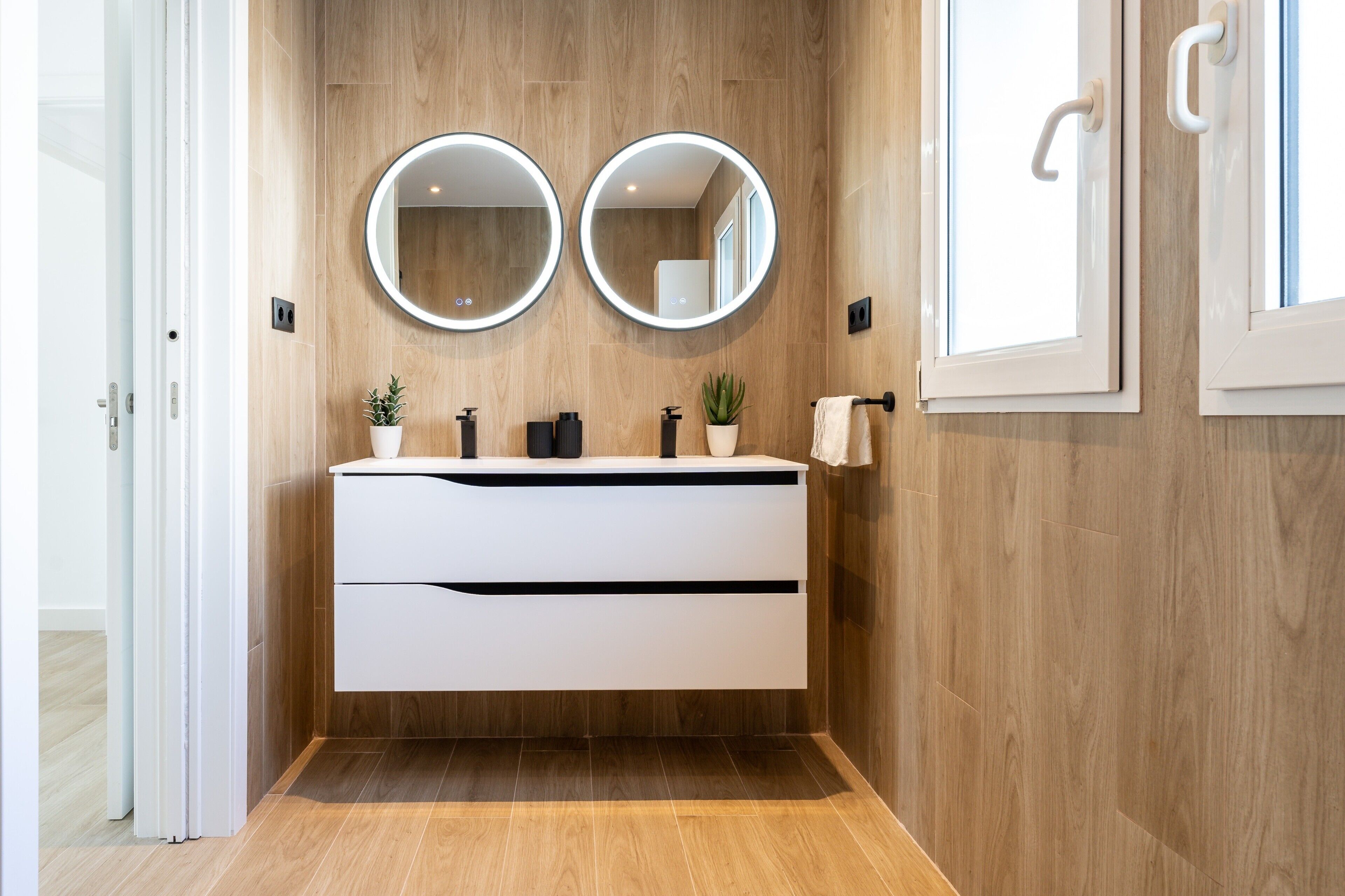 Une salle de bain moderne avec des murs en bois, un meuble-lavabo blanc, deux miroirs ronds, une plante en pot et un porte-serviettes.