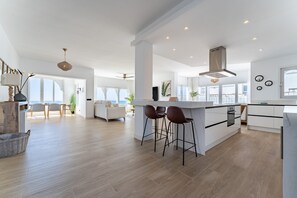 A modern kitchen with a central island, bar stools, and a view to the outside.
