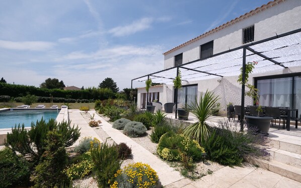 Un espace piscine extérieur moderne, doté d’une terrasse, de coins salon et d’une variété de plantes.