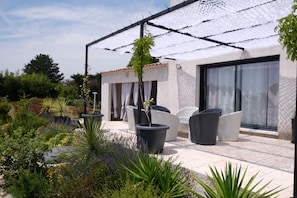 A modern outdoor patio with a pergola, seating area, and lush garden.