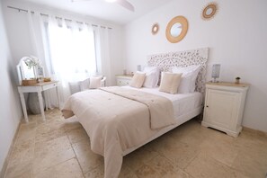 Une chambre à coucher avec un grand lit, une table de chevet, une commode, une coiffeuse avec un miroir et des œuvres d’art décoratives au mur.