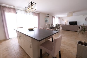 A modern kitchen with a central island, dining area with chairs, a sofa, and a TV.