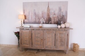Une console en bois sur laquelle est posée une toile représentant un paysage urbain, ainsi qu’une lampe et divers objets décoratifs.