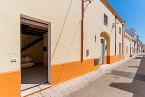 A building with an open doorway leading to a staircase, a small bed, and a tiled floor.