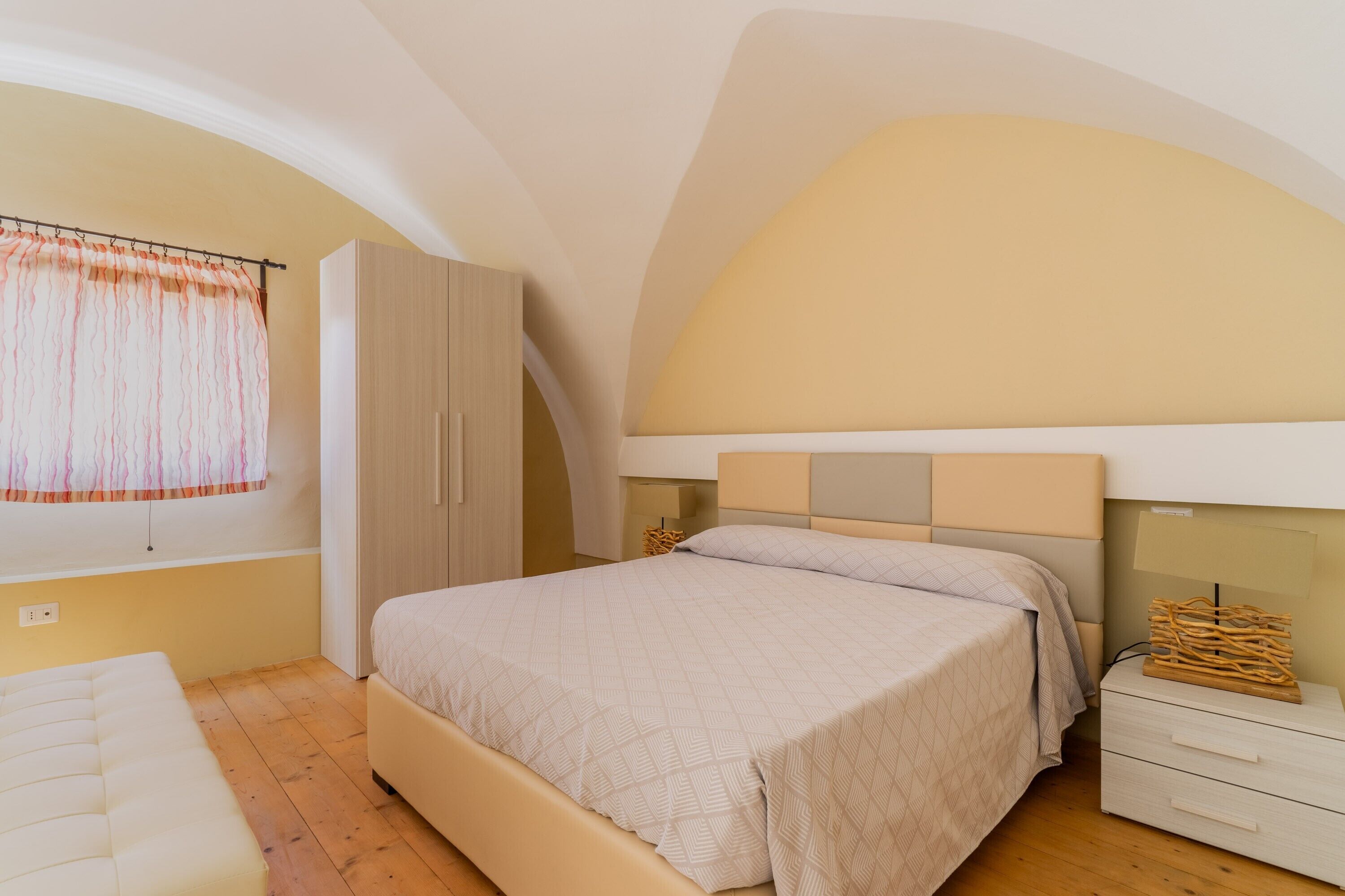 A bedroom with a bed, a wardrobe, a nightstand, and a window with curtains.