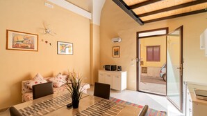 A dining area with a table, chairs, and a sofa. There is a kitchen area with a microwave and cabinets. The room has a wooden ceiling and a sliding glass door leading outside. - Apartment 'Simone' with Wi-Fi and Air Conditioning (alezio)