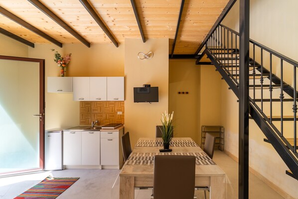 A modern kitchen with white cabinets, a wooden ceiling, and a black staircase.