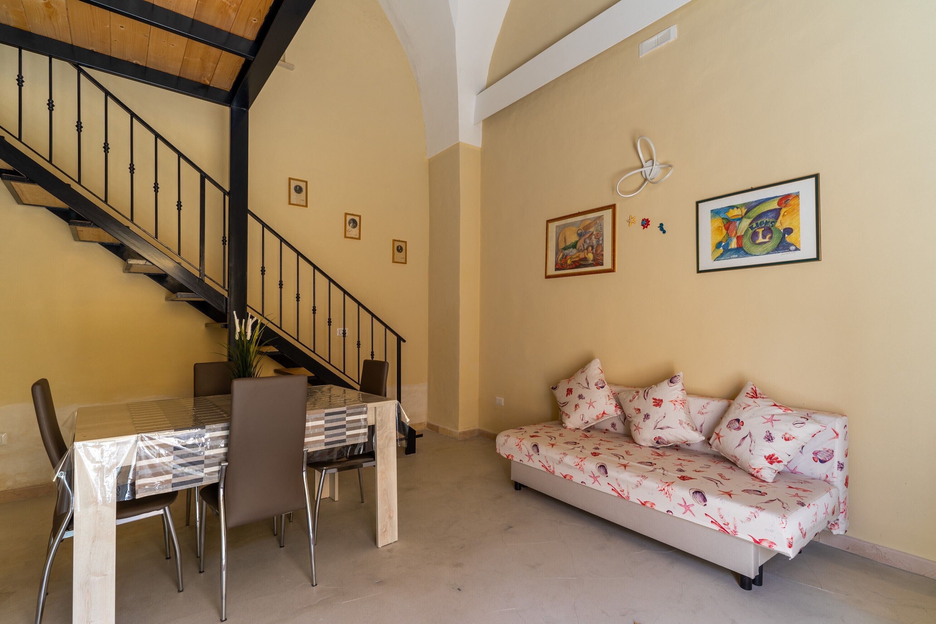 Un espace repas comprenant une table et des chaises, un canapé, un escalier et des œuvres d’art accrochées au mur.