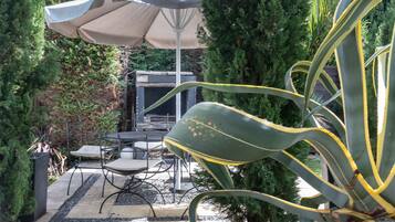 An outdoor patio with a table and chairs, surrounded by greenery and a large umbrella.