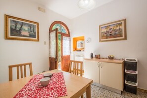 A dining area with a table, chairs, a red patterned tablecloth, and a kitchen area with cabinets and a sink.