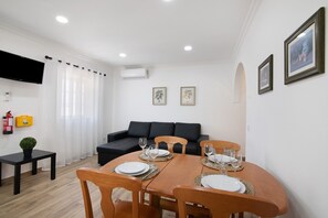 A dining area with a table set for four, a black sofa, and a flat-screen TV mounted on the wall.