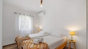 Hotellihuone, jossa on kaksi sänkyä, puulattia, lattiavalaisin ja ikkuna, jossa on verhot.