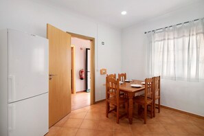 A dining area with a wooden table and chairs, a white refrigerator, and a wooden door leading to another room.