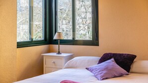 Un dormitorio con una cama, una mesita de noche, una lámpara y una ventana con vistas a árboles.