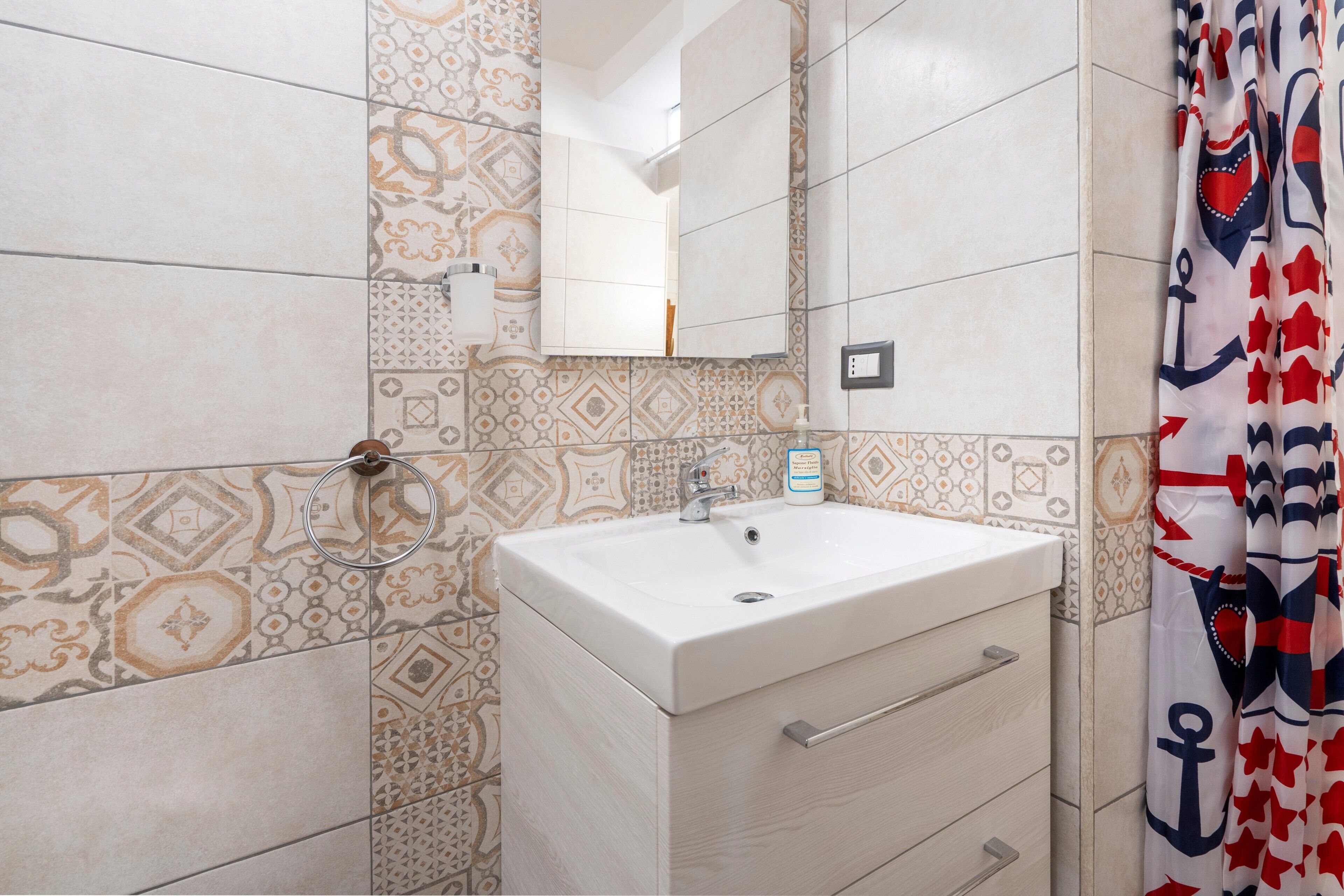 A bathroom with patterned tiles, a white sink, a mirror, and a shower curtain with nautical designs.