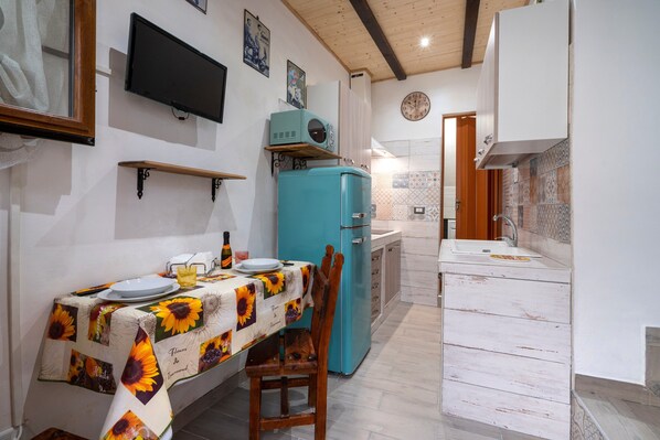 A dining area with a table set for two, a blue refrigerator, and a kitchen area with a sink and cabinets.