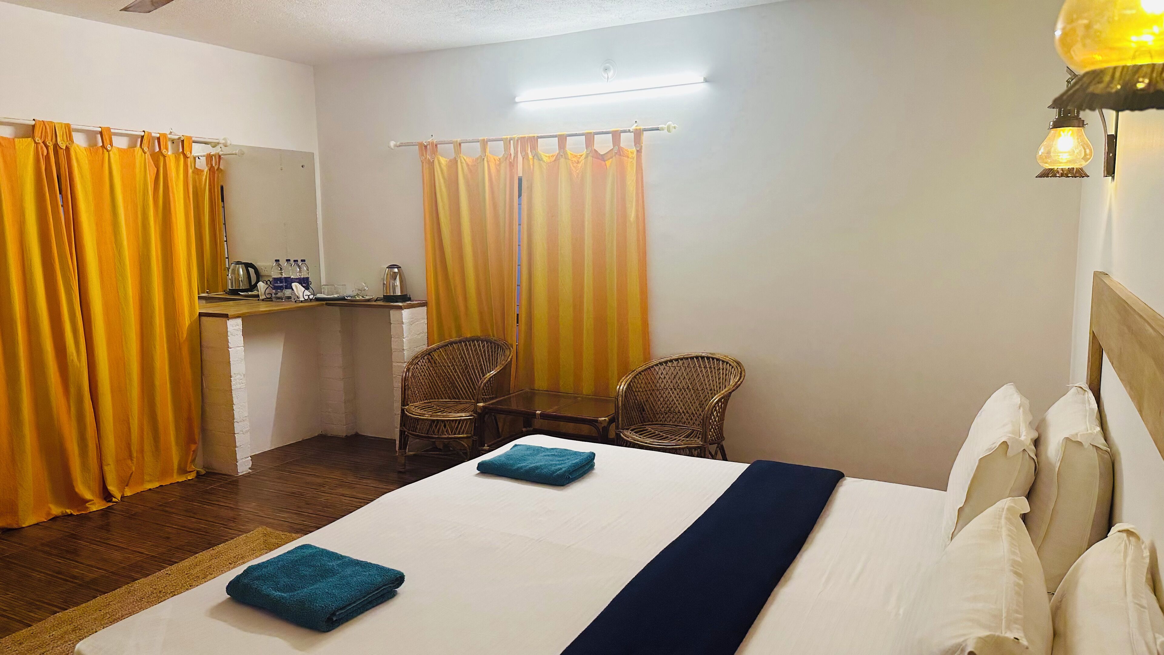 A hotel room with a bed, two chairs, a small table, a desk with a kettle, and curtains.