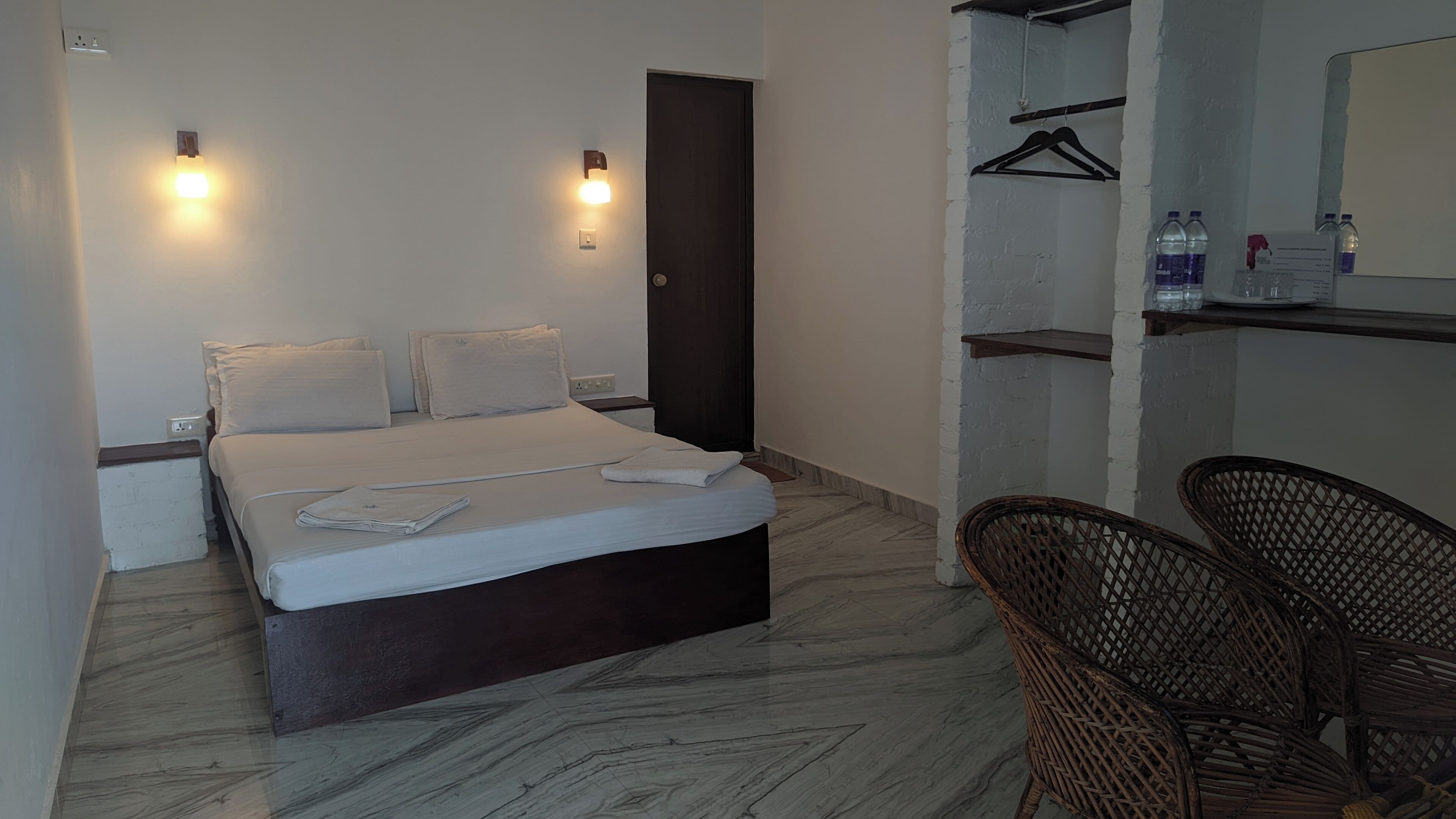 Een hotelkamer met een bed, twee nachtkastjes, een stoel, een kledingkast en een spiegel.