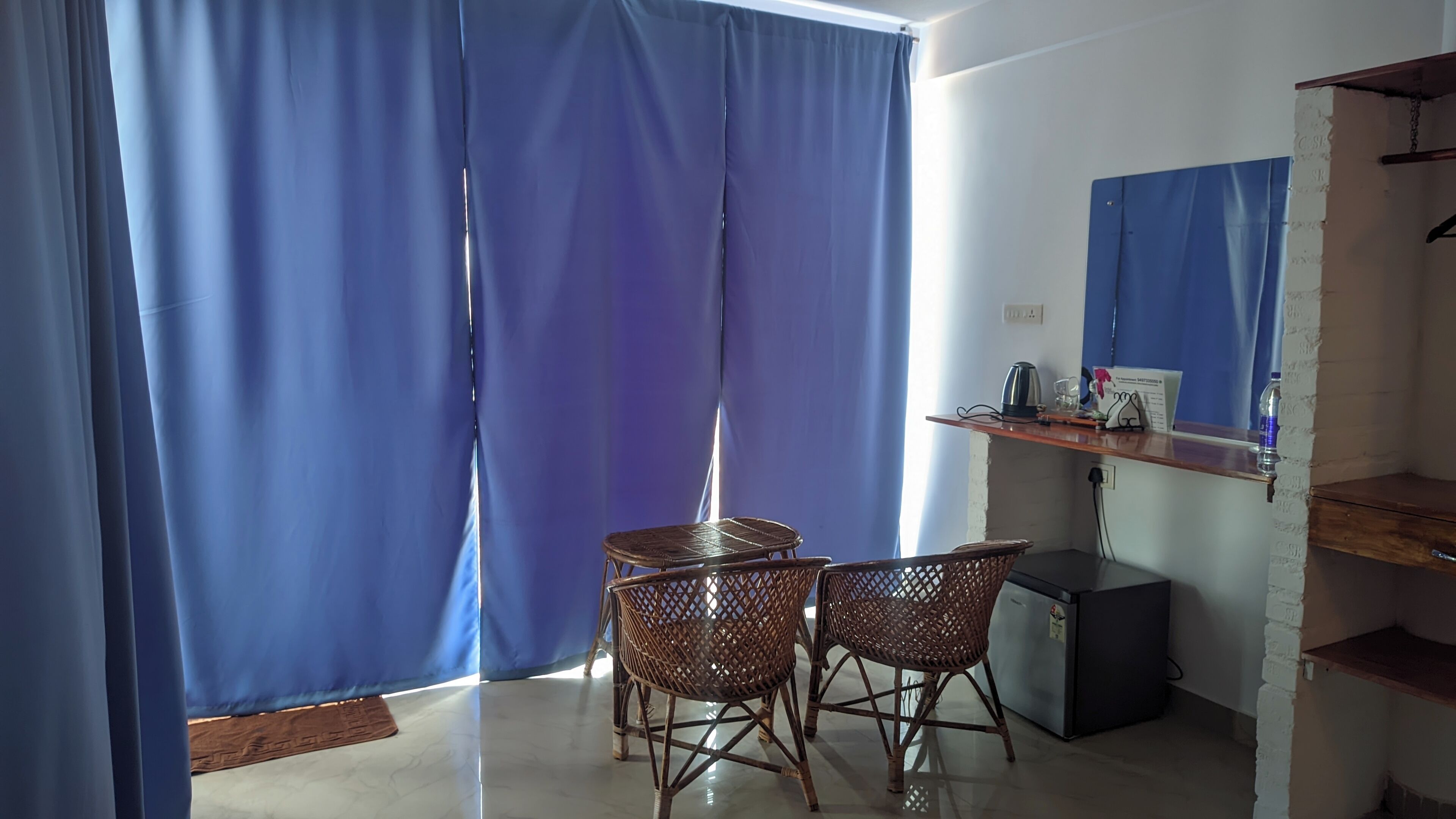 A room with a dining table and chairs, a small refrigerator, and a shelf with items.