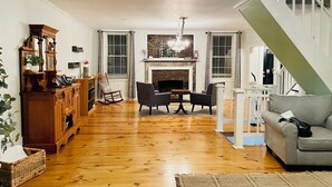 A spacious living room with hardwood flooring, a fireplace, a dining area, and a staircase.