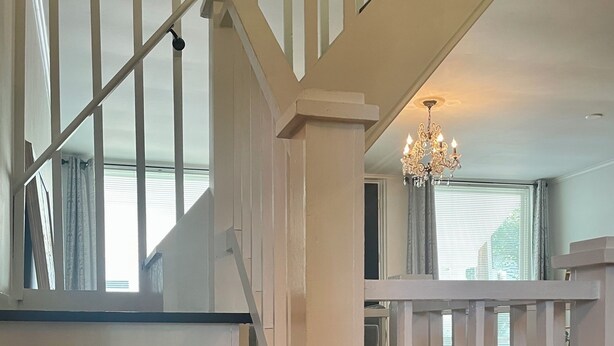 A staircase with white railings and black steps, leading to a room with a chandelier.