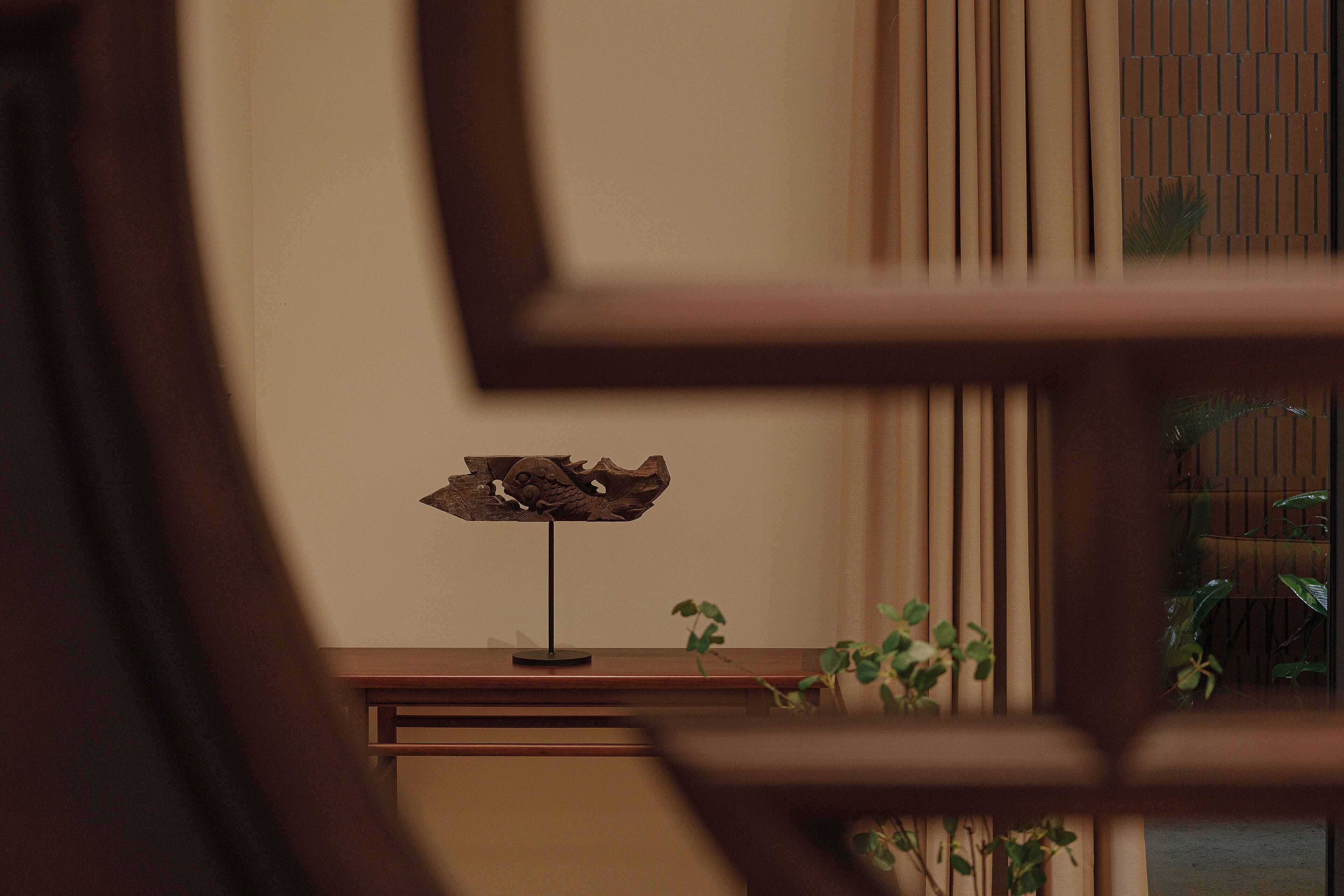 A wooden table with a decorative object on it, a plant, and a window with blinds.