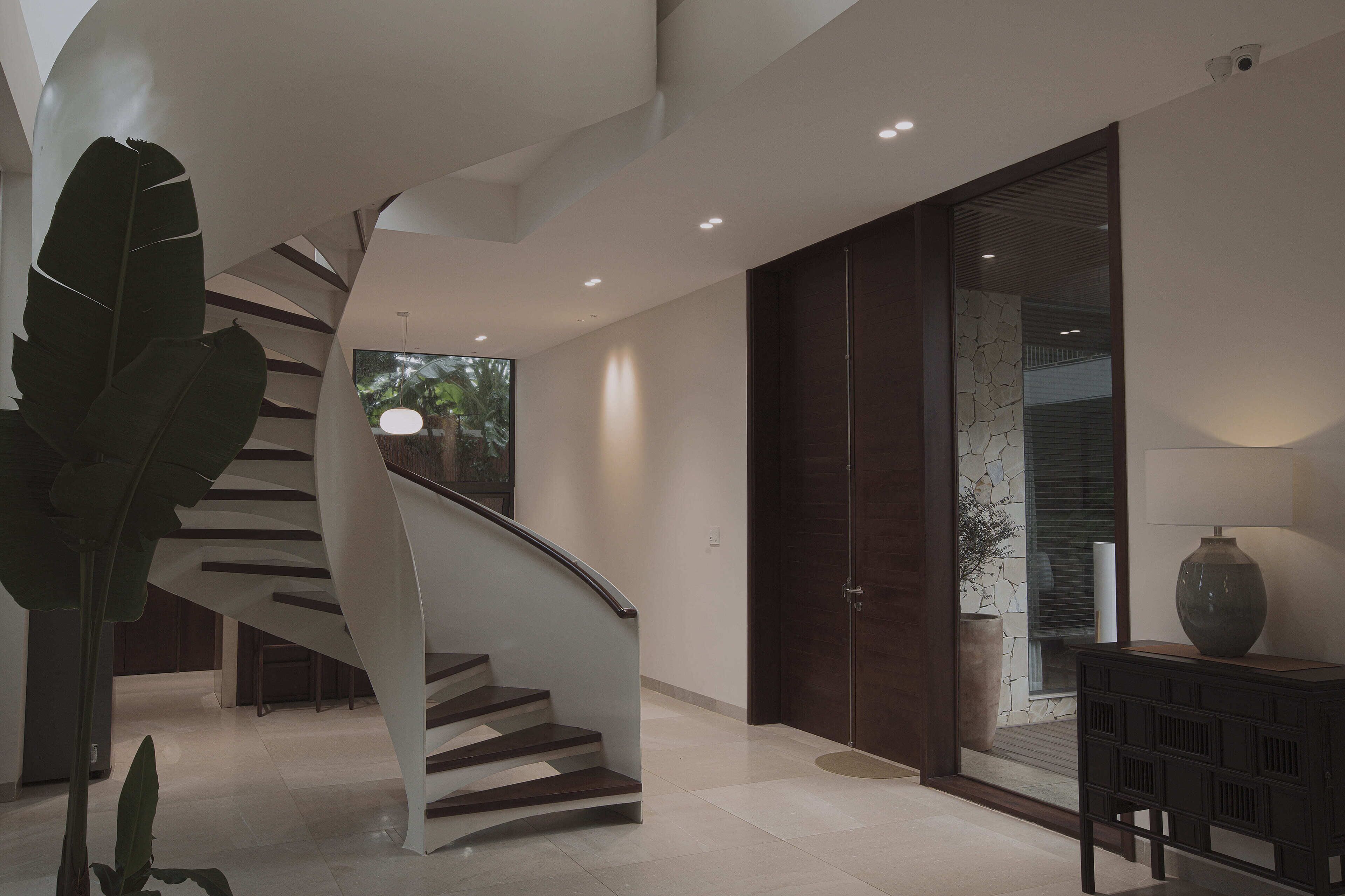 Ein modernes Interieur mit einer Wendeltreppe, einem großen Topfpflanzen und einem schlichten Konsolentisch.