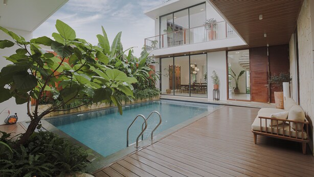 A modern outdoor pool area with a wooden deck, a lounge chair, and a glass balustrade overlooking a garden. - Nhan Stay (Hue)