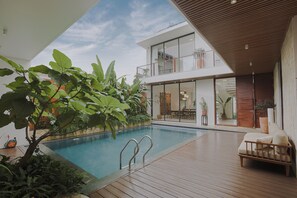 A modern outdoor pool area with a wooden deck, a lounge chair, and a glass balustrade overlooking a garden. - Nhan Stay (Hue)