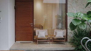 A wooden door, two wicker chairs with cushions, and a stone wall with a large plant. - Nhan Stay (Hue)