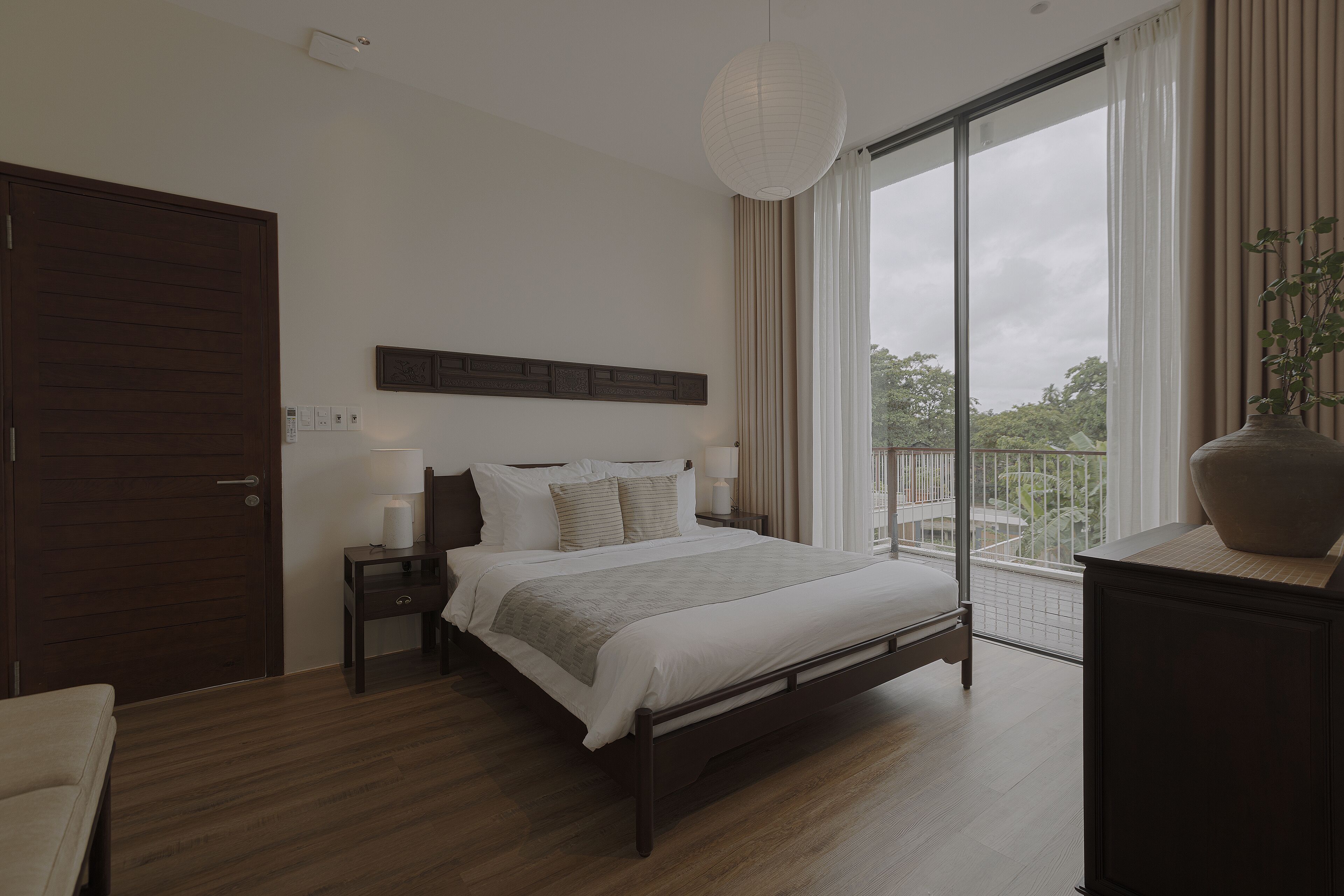 Une chambre moderne avec un grand lit, une table de chevet, une commode, une armoire et une vue sur l’extérieur grâce à une grande fenêtre.