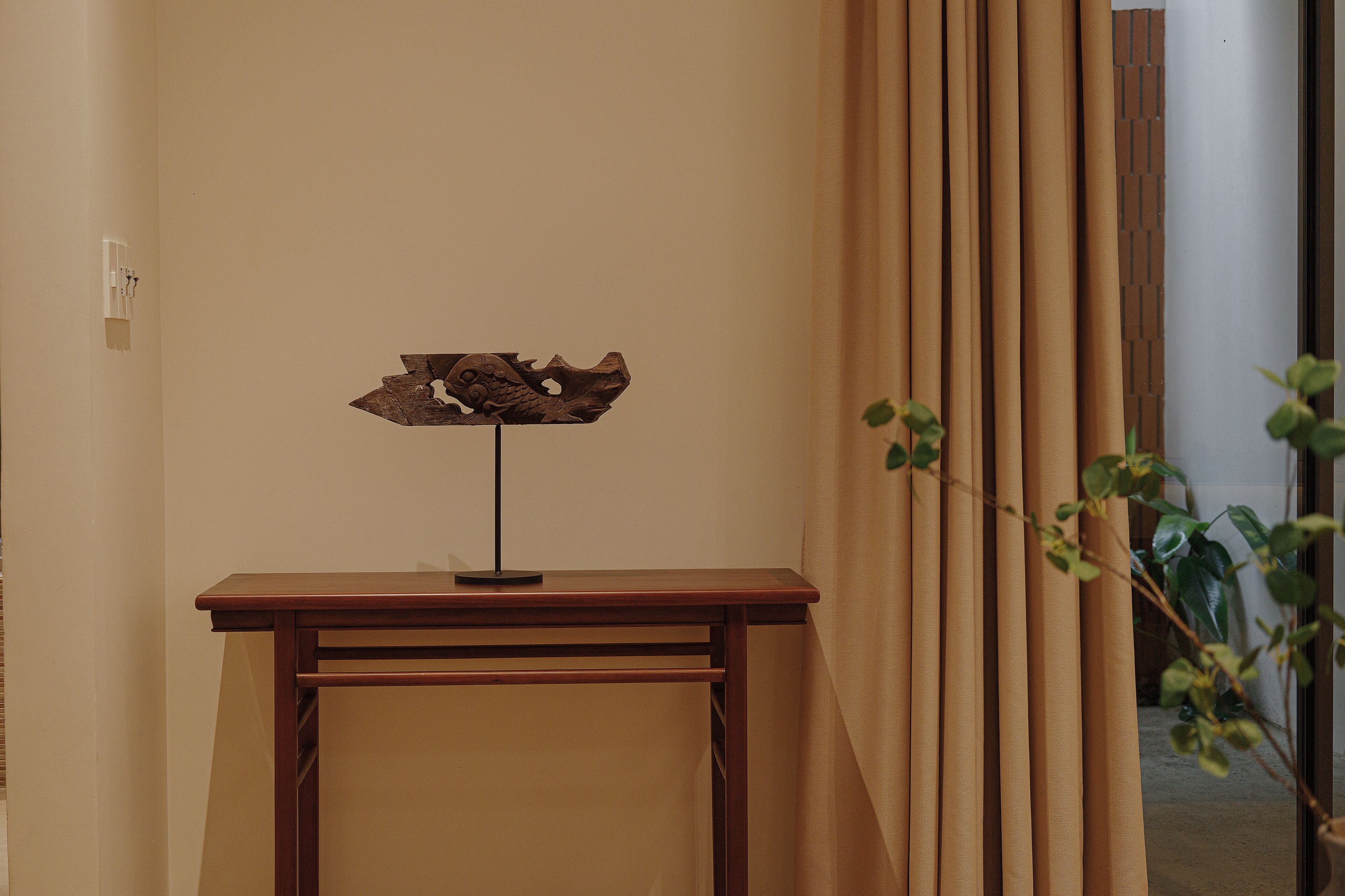 A wooden desk with a decorative piece, beige curtains, and a potted plant.