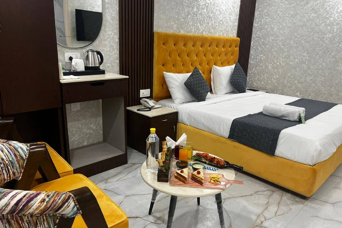 Habitación de hotel con cama, escritorio, silla y una pequeña mesa con comida y bebidas.