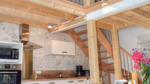 A rustic kitchen with wooden beams, a stone wall, and a modern stove. - Charming Cottage in Orchard with Modern Amenities & Scenic Views (Joué-lès-Tours)