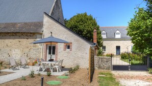 A stone house with a sloped roof, a patio with outdoor furniture, and a gated entrance. - Charming Cottage in Orchard with Modern Amenities & Scenic Views (Joué-lès-Tours)