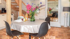 A dining area with a table set for four, a vase of flowers, and a staircase leading to an upper level. - Charming Cottage in Orchard with Modern Amenities & Scenic Views (Joué-lès-Tours)
