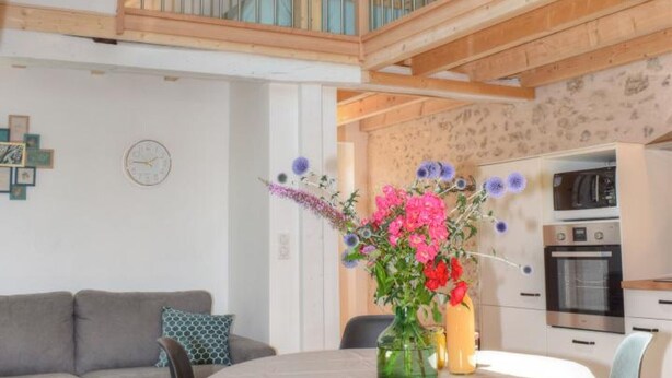 A modern kitchen with built-in appliances, a dining area with a round table, and a loft bedroom with a glass railing. - Charming Cottage in Orchard with Modern Amenities & Scenic Views (Joué-lès-Tours)