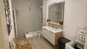 A modern bathroom with a glass shower enclosure, a white sink with a mirror above, and a wicker chair. - Quiet downtown apartment (Rodez)