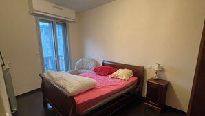 A bedroom with a bed, bedside table, and a window. - Quiet downtown apartment (Rodez)