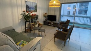A modern living room with a sofa, chairs, a TV, and a large window with a balcony view. - Quiet downtown apartment (Rodez)