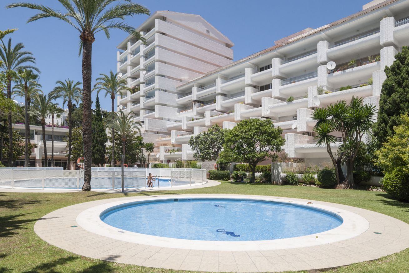 A hotel with a swimming pool surrounded by palm trees and a large building with multiple balconies.