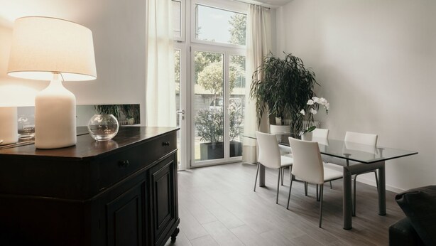 A modern dining area with a glass table, white chairs, a dark wooden cabinet, and a large window with curtains. - GuestHost - Studio 1 is the best you could wish for in Bologna, a comfortable and beautiful home. It's a spacious, renovated and stylishly furnished two-room apartment, bright and airy, perfect for a couple or four friends. It's close to the highway and  (Bologna)